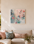 An abstract painting with soft pink, teal, and red brushstrokes hangs on a beige wall above a cream sectional sofa styled with patterned pillows and a throw blanket in a bright, modern living room.