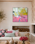 A bright, modern living room with a white sectional sofa, colorful patterned pillows, a rustic wooden coffee table, a stone fireplace, and a vibrant abstract painting hanging on the wall.